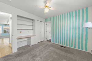 Unfurnished bedroom with carpet floors, wallpapered walls, ceiling fan, built in study area, and a closet