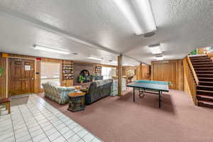Recreation room with carpet flooring, wood walls, tile patterned flooring, and a textured ceiling