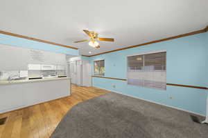 Unfurnished living room with ornamental molding, ceiling fan, light wood-style floors, and a textured ceiling