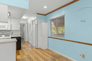 Kitchen featuring light countertops, ornamental molding, white appliances, white cabinets, and light wood-type flooring