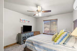 Carpeted bedroom featuring a wall mounted air conditioner and a ceiling fan