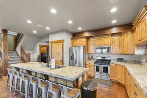 Kitchen featuring recessed lighting, appliances with stainless steel finishes, a breakfast bar area, an island with sink, and light stone counters