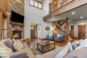 Living room with hardwood / wood-style floors, a high ceiling, stairway, a stone fireplace, and recessed lighting