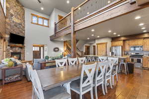 Dining room with a stone fireplace, stairway, dark wood-type flooring, recessed lighting, and a high ceiling