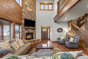 Living area featuring a towering ceiling, hardwood / wood-style floors, a stone fireplace, and stairs