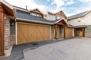 Craftsman-style house with stone siding, roof with shingles, and driveway