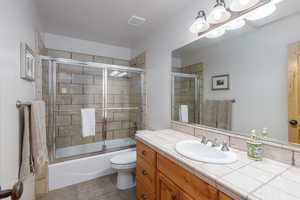 Bathroom with vanity, bath / shower combo with glass door, a textured ceiling, and light tile patterned floors