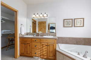 Ensuite bathroom with double vanity, a tub with jets, and light tile patterned floors
