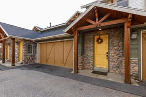 Entrance to property with stone siding, a garage, and a shingled roof