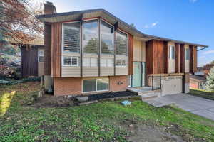 View of front facade featuring brick siding, a garage, driveway, and a chimney