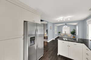 Kitchen with stainless steel refrigerator with ice dispenser, dark stone counters, white cabinetry, wood finish floors, and lofted ceiling