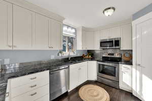 Kitchen featuring appliances with stainless steel finishes, dark stone countertops, dark wood-style floors, and white cabinetry