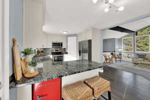 Kitchen featuring stainless steel appliances, decorative backsplash, white cabinets, a peninsula, and dark wood-style flooring
