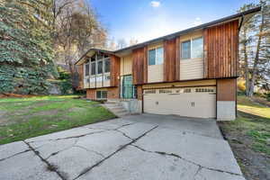 Bi-level home featuring driveway, brick siding, an attached garage, and a front yard