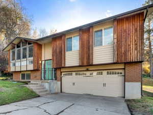 Bi-level home featuring driveway, Cedar siding, an attached garage, and a front yard