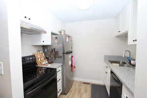 Kitchen featuring black appliances, white cabinetry, under cabinet range hood, and light stone counters