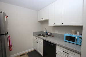 Kitchen featuring dishwasher, white cabinets, freestanding refrigerator, and light stone countertops
