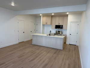 Kitchen with light wood finish cabinetry, stainless steel appliances, light wood-style floors, an island with sink, and light stone countertops