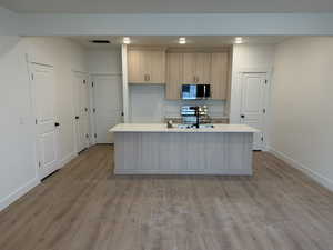 Kitchen with light brown cabinetry, appliances with stainless steel finishes, an island with sink, and light wood-style floors