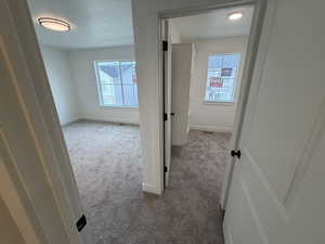 Corridor with light carpet, healthy amount of natural light, and a textured ceiling