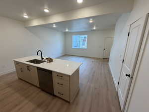 Kitchen with light brown cabinetry, open floor plan, dishwasher, light stone counters, and light wood-style flooring