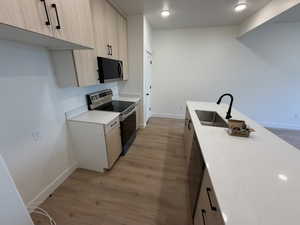 Kitchen with light brown cabinets, stainless steel appliances, light stone countertops, light wood-style floors, and modern cabinets