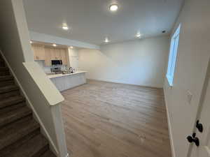 Kitchen featuring light brown cabinetry, a peninsula, light wood-style floors, stainless steel appliances, and a kitchen bar