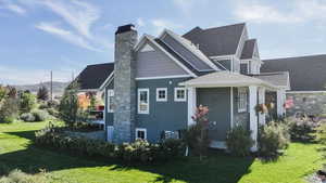 View of side of home featuring a yard, a chimney, and a shingled roof