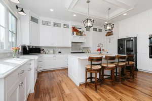 Kitchen with a breakfast bar area, hanging light fixtures, black appliances, a center island, and white cabinets