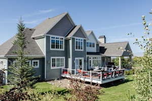Rear view of property with a shingled roof, a deck, and a lawn