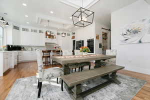 Dining area featuring a barn door, light wood-style flooring, a tray ceiling, recessed lighting, and a chandelier