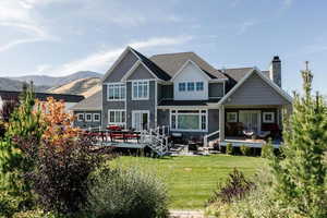 Back of house featuring a lawn, a chimney, a deck, and a shingled roof