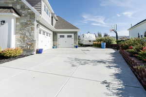 View of side of property featuring stone siding, concrete driveway, a garage, and a shingled roof