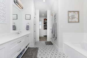Bathroom with a walk in closet, vanity, a garden tub, and recessed lighting