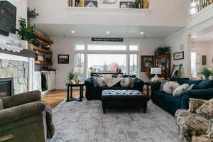 Living area featuring a stone fireplace, a high ceiling, light wood-style floors, and recessed lighting