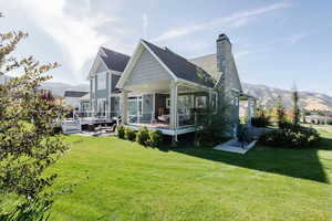 Back of house featuring a lawn, a deck with mountain view, and a chimney