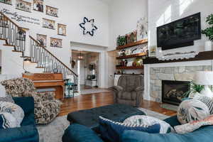 Living area featuring wood finished floors, stairs, a stone fireplace, a high ceiling, and a chandelier