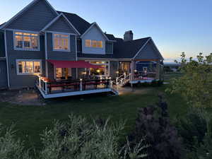 Back of property at dusk featuring a wooden deck, a yard, a chimney, and board and batten siding