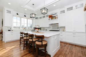Kitchen featuring white cabinetry, glass insert cabinets, a kitchen bar, and recessed lighting