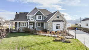 Craftsman-style house featuring stone siding, a front yard, a chimney, roof with shingles, and a standing seam roof