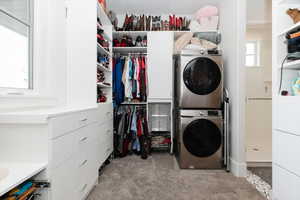 Laundry area featuring stacked washer / dryer and light colored carpet