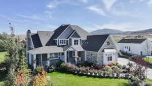 Craftsman house featuring stone siding, a front yard, a chimney, covered porch, and a mountain view