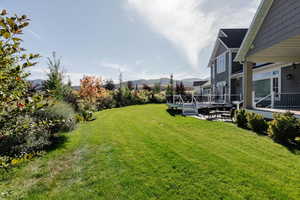 View of grassy yard with a deck with mountain view