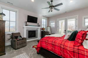 Carpeted bedroom featuring access to exterior, a ceiling fan, a tiled fireplace, recessed lighting, and french doors