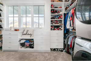Spacious closet featuring stacked washing machine and dryer and light colored carpet