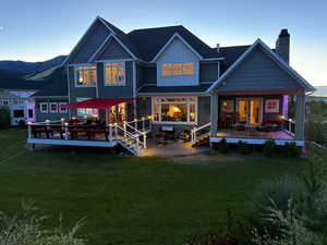 Rear view of house featuring board and batten siding, a deck, a patio area, a yard, and a chimney