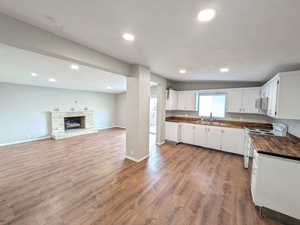 Kitchen with white cabinets, white range with electric stovetop, dark wood-style flooring, a stone fireplace, and recessed lighting