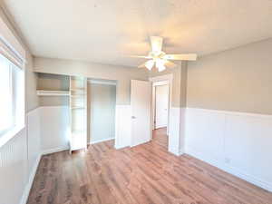 Bedroom featuring wood finished floors, a textured ceiling, wainscoting, a closet, and ceiling fan