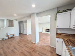 Kitchen with white cabinetry, butcher block counters, light wood-style flooring, recessed lighting, and a stone fireplace