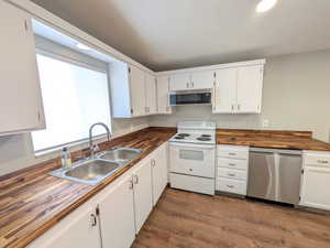 Kitchen featuring stainless steel appliances, butcher block countertops, white cabinets, dark wood-style flooring, and recessed lighting